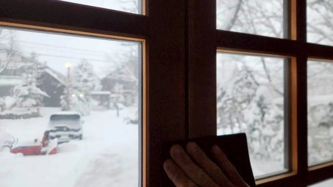 一隻手擦著木窗，窗外是白馬村雪後的街道與停放的汽車
